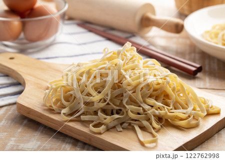 Close up Chinese flat egg noodle on wooden board,Flat yellow noodles covered by flour on wood table. Close up Chinese flat egg noodle on wooden board,Flat yellow noodles covered by flour on wood table. 122762998
