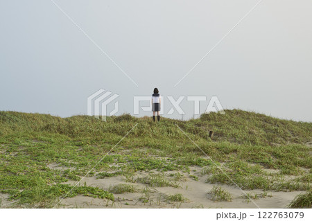 草原に立つ女子高校生の後ろ姿 122763079