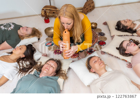 Group therapy session with Tibetan singing bowls for group of women lying on wooden floor surrounded by copper bowls. Meditation and relaxation 122763867