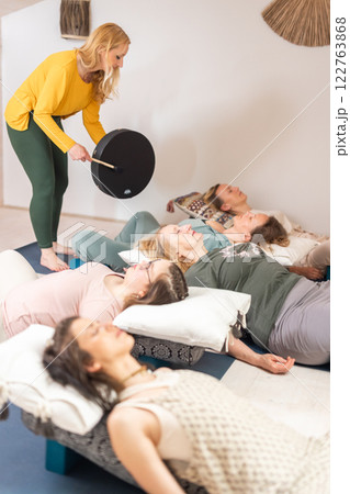 Group therapy session with Tibetan drum for group of women lying on wooden floor surrounded by copper bowls. Meditation and relaxation Group therapy session with Tibetan drum for group of women lying on wooden floor surrounded by copper bowls. Meditation and relaxation 122763868