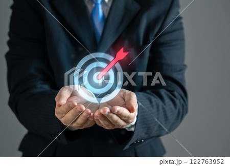 Businessman holding an arrow at a target. Concept of a goal and its achievement. Achieving objectives, business strategy, career ambitions, success planning, financial targets Businessman holding an arrow at a target. Concept of a goal and its achievement. Achieving objectives, business strategy, career ambitions, success planning, financial targets 122763952