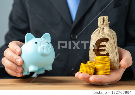 Businessman holds a piggy bank and a bag of money. Putting aside part of the profit for retirement or savings. Wealth management, investment strategies. Pension funds, financial stability Businessman holds a piggy bank and a bag of money. Putting aside part of the profit for retirement or savings. Wealth management, investment strategies. Pension funds, financial stability 122763994