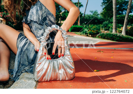 Close-up of a metallic handbag paired with bold red nails, capturing modern elegance and luxury 122764072