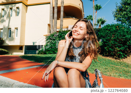 Bright and cheerful: a young woman on the phone in front of a stylish property, blending tech, joy 122764080