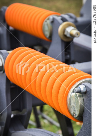 Orange hard spring made of steel. Part of big industrial or agricultural machine Orange hard spring made of steel. Part of big industrial or agricultural machine 122765989