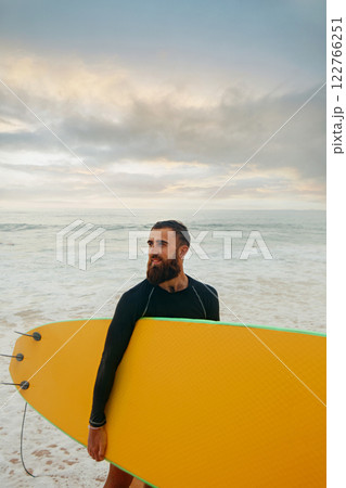 Smiling young man with surfboard on the beach. Boy coming out of the ocean after water surfing. 122766251