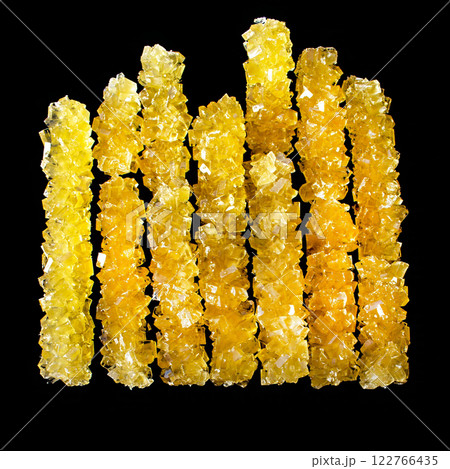 A row of yellow sticks with a black background. The sticks are made of sugar and are arranged in a line 122766435