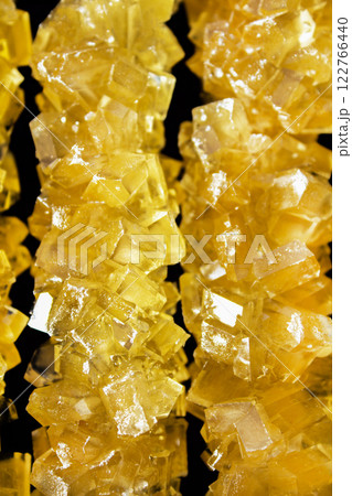 The sticks are made of sugar and are arranged in a line. A row of yellow crystals are lined up on a black surface. The crystals are all different sizes and shapes 122766440