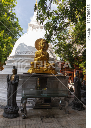 Sitting Buddha, golden statue placed in front of white pagoda 122766988