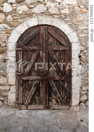 Old dark brown wooden door with arch is in an ancient stone wall 122766991