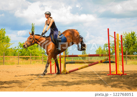 Jockey young girl doing horse jumping through hurdle Jockey young girl doing horse jumping through hurdle 122768051