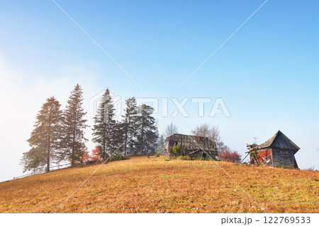 Sunrise above the high mountain foggy valley with old wooden houses on a hill in a mountain forest 122769533