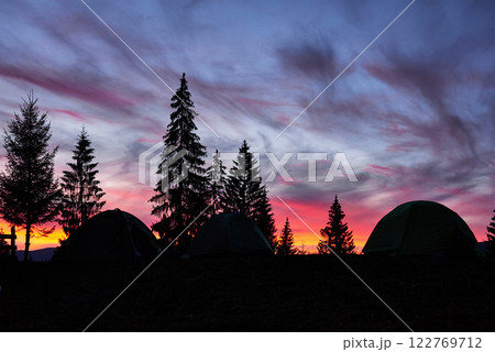Majestic sky, pink cloud against the silhouettes of pine trees in the twilight time, tents on the front. Carpathians, Ukraine, Europe. Discover the world of beauty 122769712