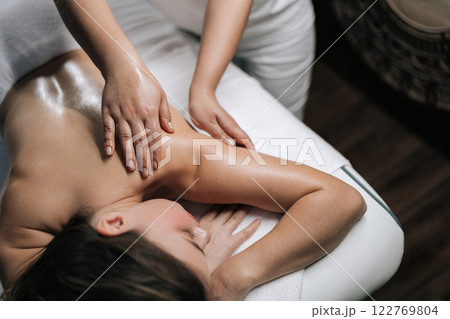 Top view of unrecognizable massage therapist smoothing fragrant oil across woman client back during tranquil wellness spa treatment, promoting relaxation and stress relief. Concept of luxury massage. Top view of unrecognizable massage therapist smoothing fragrant oil across woman client back during tranquil wellness spa treatment, promoting relaxation and stress relief. Concept of luxury massage. 122769804
