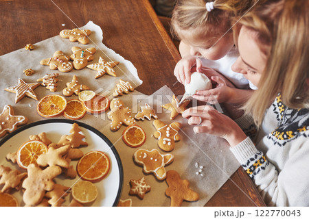 Mom and daughter decorate the Christmas cookie with white sugar 122770043