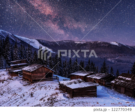 magical winter snow covered trees and mountain village. Winter landscape. Vibrant night sky with stars and nebula and galaxy. magical winter snow covered trees and mountain village. Winter landscape. Vibrant night sky with stars and nebula and galaxy. 122770349