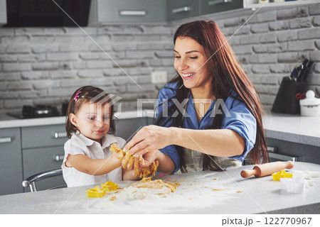 Happy family in the kitchen. Holiday food concept. Mother and daughter preparing the dough, bake cookies. Happy family in making cookies at home. Homemade food and little helper Happy family in the kitchen. Holiday food concept. Mother and daughter preparing the dough, bake cookies. Happy family in making cookies at home. Homemade food and little helper 122770967