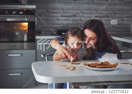 Happy family in the kitchen. Holiday food concept. Mother and daughter decorate cookies. Happy family in making homemade pastry. Homemade food and little helper Happy family in the kitchen. Holiday food concept. Mother and daughter decorate cookies. Happy family in making homemade pastry. Homemade food and little helper 122771012