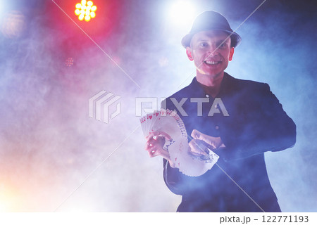 Magician showing trick with playing cards. Magic or dexterity, circus, gambling. Prestidigitator in dark room with fog Magician showing trick with playing cards. Magic or dexterity, circus, gambling. Prestidigitator in dark room with fog 122771193