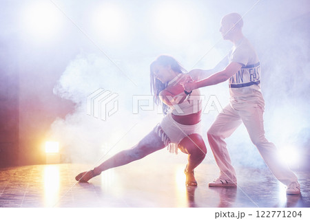 Skillful dancers performing in the dark room under the concert light and smoke. Sensual couple performing an artistic and emotional contemporary dance 122771204