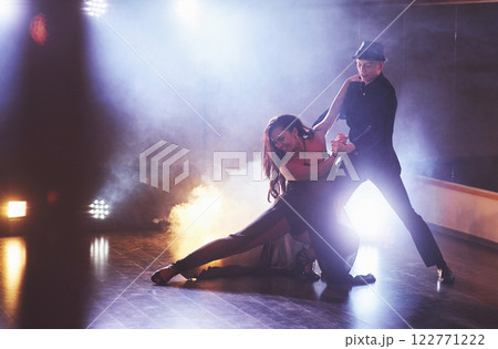 Skillful dancers performing in the dark room under the concert light and smoke. Sensual couple performing an artistic and emotional contemporary dance Skillful dancers performing in the dark room under the concert light and smoke. Sensual couple performing an artistic and emotional contemporary dance 122771222