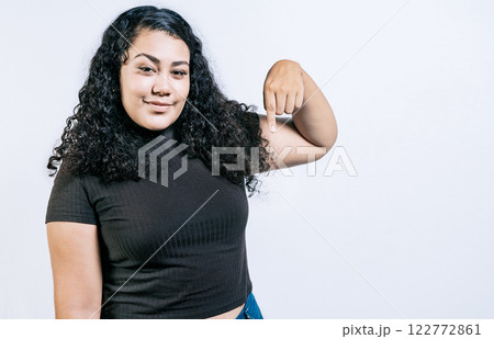Attractive latin girl pointing down an advertisement. Latin people pointing down at a banner. Young woman pointing advertising down 122772861