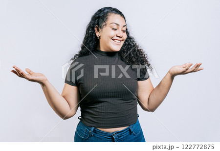 Smiling latin woman comparing with palms hands isolated. Happy girl balancing product with palms isolated 122772875