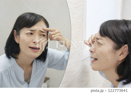 鏡でおでこの皺を見て悩む50代女性 鏡でおでこの皺を見て悩む50代女性 122773641