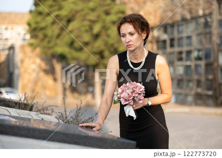 Sorrowful woman in black standing with flowers by grave Sorrowful woman in black standing with flowers by grave 122773720