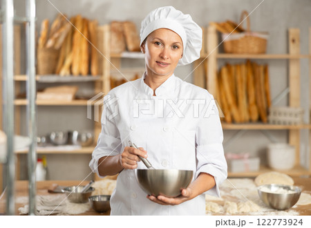 Woman baker cook stands against background of workspace with bowl and whisk 122773924
