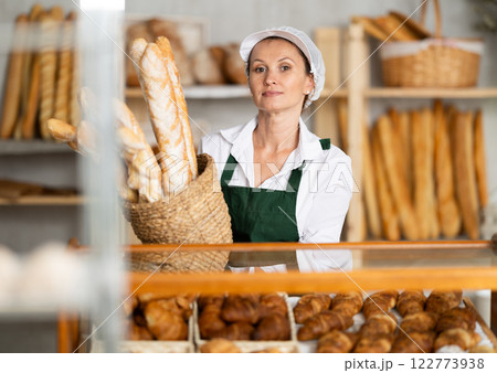Female baker worker sells baguette, shows many products 122773938