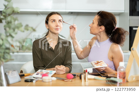 Woman applying soft shade of eyeshadow to friend eyelids Woman applying soft shade of eyeshadow to friend eyelids 122773950