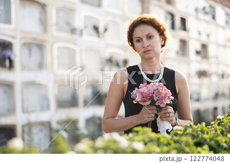 Upset woman in black dress, who lost loved one, brings flowers to grave 122774048
