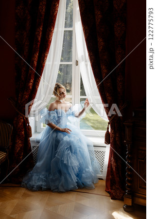Portrait of an elegant woman in a light blue ball gown in a classic interior by a large window Portrait of an elegant woman in a light blue ball gown in a classic interior by a large window 122775793