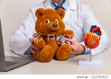 Male doctor wears white medical gown suit work in hospital clinic office hold teddy bear toy check heart beat with stethoscope. Health care medicine concept Male doctor wears white medical gown suit work in hospital clinic office hold teddy bear toy check heart beat with stethoscope. Health care medicine concept 122783427