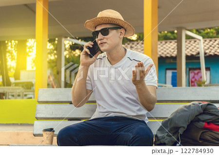 An attractive guy calling on a cell phone on a bench, a man sitting on a bench calling on the phone. 122784930