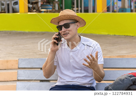 An attractive guy calling on a cell phone on a bench, a man sitting on a bench calling on the phone. 122784931