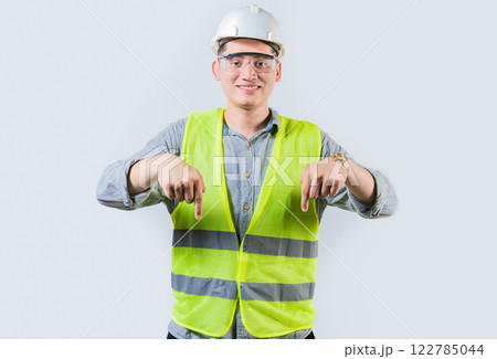 Smiling engineer pointing advertising down isolated. Smiling friendly engineer pointing down isolated 122785044