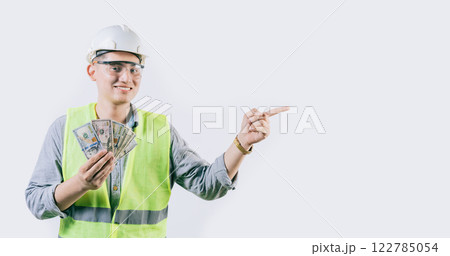 Smiling young engineer holding money pointing aside isolated. Handsome male engineer showing money pointing an advertisement isolated Smiling young engineer holding money pointing aside isolated. Handsome male engineer showing money pointing an advertisement isolated 122785054