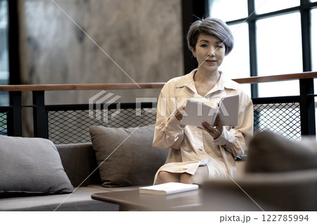 Elder woman is sitting on the sofa reading a book 122785994