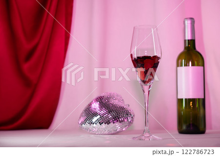 Wine glass with heart confetti, bottle, and disco on pink background 122786723