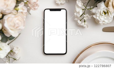花のテーブルセッティングにスマートフォンを置いたミニマリストな結婚式招待状のモックアップ 122786807