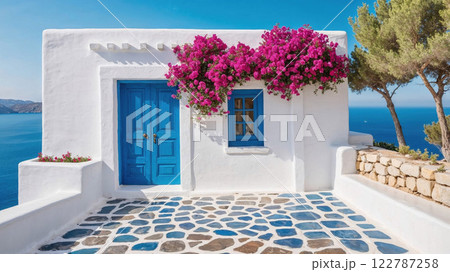 white Greek house adorned with vibrant pink bougainvillea, set against a crystal-clear blue sky and overlooking the sea, capturing Mediterranean charm 122787258
