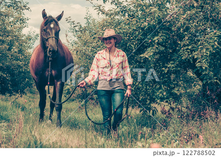 Western woman walking on green meadow with horse Western woman walking on green meadow with horse 122788502
