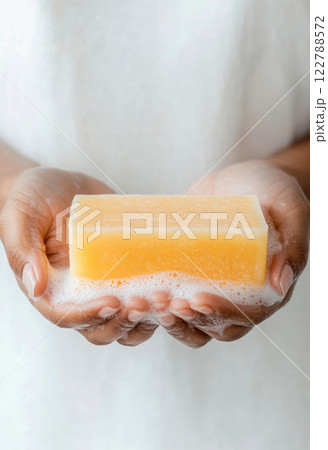 Close-up of hands holding rectangular orange-yellow craft soap, with foam on palms, advertisement of soap from local handmade soap factory Close-up of hands holding rectangular orange-yellow craft soap, with foam on palms, advertisement of soap from local handmade soap factory 122788572