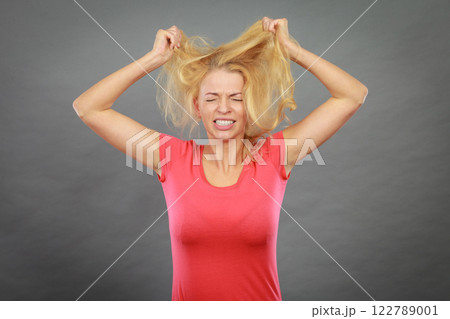 Frustrated woman holding her damaged blonde hair 122789001