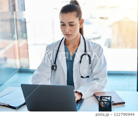 Doctor typing on a laptop in an office writing a proposal or on a video call using telemedicine. Young healthcare professional or GP using the internet for research or online consultation 122790944