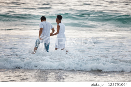 Love, beach and travel couple happy walking in water, by the ocean or waves together bonding on holiday or vacation. Man and woman holding hands during honeymoon smiling in the sea. Love, beach and travel couple happy walking in water, by the ocean or waves together bonding on holiday or vacation. Man and woman holding hands during honeymoon smiling in the sea. 122791064