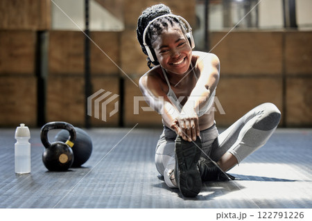 Portrait of woman stretching with music at gym, audio podcast for workout motivation and happy about fitness training on floor at health club. African athlete or sports person doing exercise 122791226