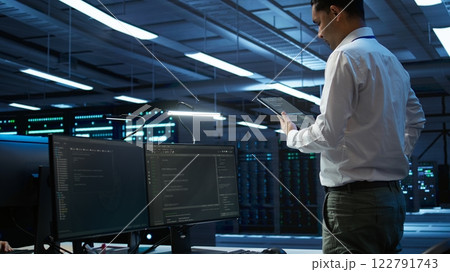 Data center engineer responsible for installation and repair of networking equipment solving tasks on device. IT professional doing maintenance on server room infrastructure using tablet, camera B 122791743